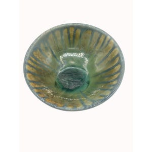 May include: A round ceramic bowl featuring a glossy glaze with a blend of sage green and earthy tan tones. The interior surface displays a radiating pattern of vertical stripes that extend from the centre towards the rim, creating a textured effect.