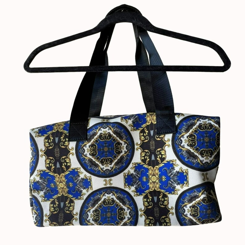 Puede incluir: Una bolsa de lona blanca y azul con estampado y correas negras. El patr&oacute;n presenta un dise&ntilde;o repetitivo de c&iacute;rculos azules y dorados con detalles intrincados.