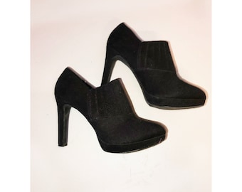 May include: A pair of black suede ankle boots with a high heel. The boots have a pointed toe and a zip on the side.