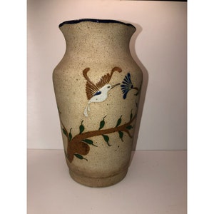 May include: A beige ceramic vase with a blue rim and a painted design of a hummingbird with green leaves and a blue flower.