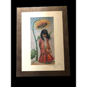 Puede incluir: Una impresión enmarcada de una pintura que representa a una niña con un vestido rojo de pie junto a un gran girasol. La niña tiene el pelo largo y negro y mira hacia abajo. La pintura está firmada "Manzella" en la esquina inferior derecha.