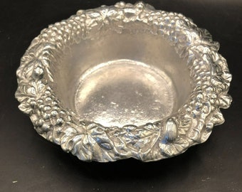 May include: A silver bowl with a grapevine design around the rim. The bowl is made of pewter and has a smooth, shiny finish.