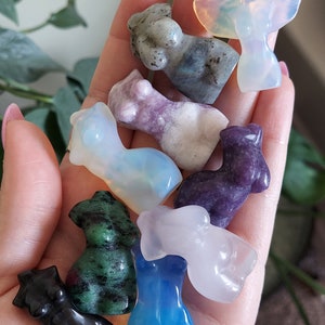 May include: A collection of eight small, carved figurines made of various gemstones. The figurines are in the shape of human figures and are in a variety of colors, including black, green, blue, purple, and white.