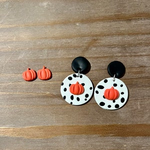 May include: A pair of dangle earrings with black and white polka dot circles and orange pumpkin charms.