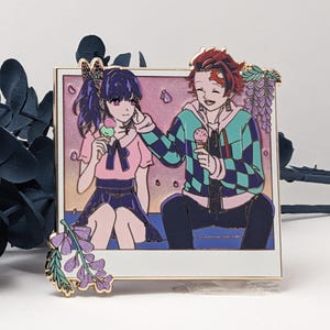 Op de afbeelding: Een gouden emaille pin met een cartoon afbeelding van twee anime-personages, een meisje met paars haar en een jongen met rood haar, die samen zitten en ijs eten. De afbeelding is geplaatst in een wit fotolijstje met een roze en paarse achtergrond. De pin heeft een bloemmotief rond de lijst.
