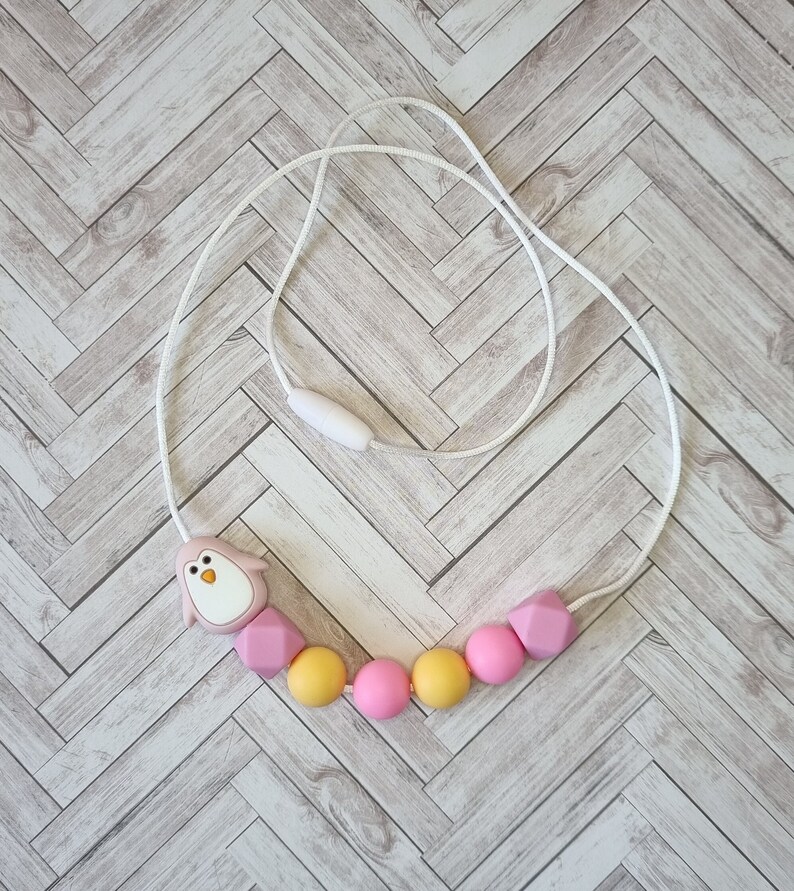 Puede incluir: Un collar de dentici&oacute;n de silicona rosa y amarillo con un dije de ping&uuml;ino. El collar est&aacute; hecho de cuentas de silicona suaves y masticables y est&aacute; dise&ntilde;ado para beb&eacute;s y ni&ntilde;os peque&ntilde;os.