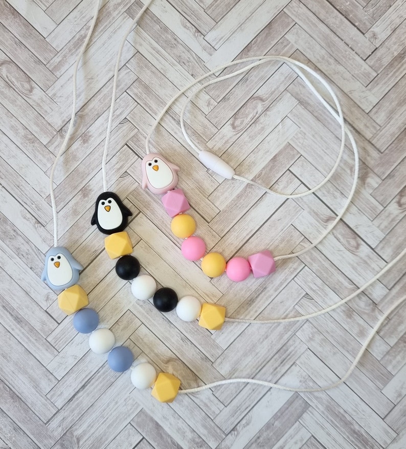 Puede incluir: Tres collares de dentici&oacute;n de silicona con dijes de ping&uuml;ino. Los collares est&aacute;n hechos con cuentas de diferentes colores, incluyendo amarillo, rosa, azul, blanco y negro.