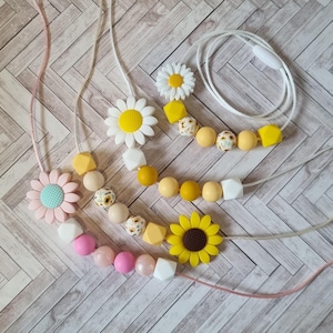May include: Four necklaces with silicone beads and flower charms. The necklaces are made with yellow, pink, white, and brown beads. The flower charms are daisies and sunflowers.