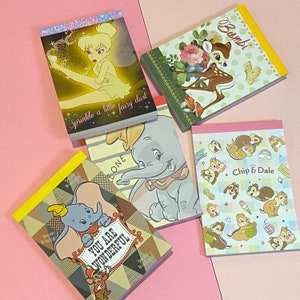 Op de afbeelding: Een set van zes kleurrijke notitieblokken met verschillende Disney-figuren. De blokken zijn versierd met afbeeldingen van Tinkerbell, Dumbo, Chip en Dale, Bambi en een bloemenontwerp. De tekst op de blokken is "Sprinkle a little fairy dust", "You are wonderful", "Chip & Dale", "Bambi" en "One".