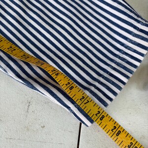 Puede incluir: Primer plano de una tela a rayas azules y blancas. Una cinta m&eacute;trica amarilla se coloca sobre la tela, mostrando medidas en cent&iacute;metros. La tela parece ser mezclilla o un material similar.