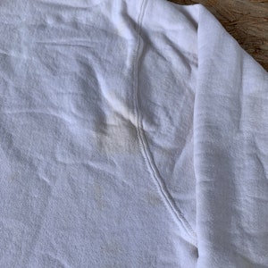 May include: White cotton sweatshirt with a slight yellow stain on the underarm.