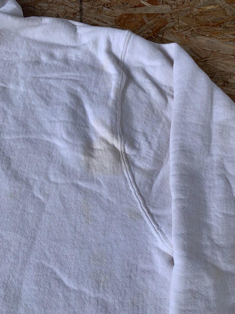 May include: White cotton sweatshirt with a slight yellow stain on the underarm.