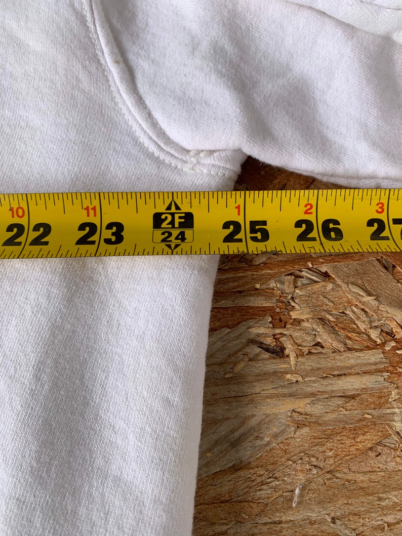 May include: Close-up of a white cotton sweatshirt with a yellow measuring tape showing 22 to 27 inches.