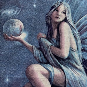 May include: A celestial-themed illustration of a fairy with long, flowing silver hair and blue wings. She is holding a glowing orb, with a starry night sky and galaxies in the background. The fairy is wearing a flowing blue gown.