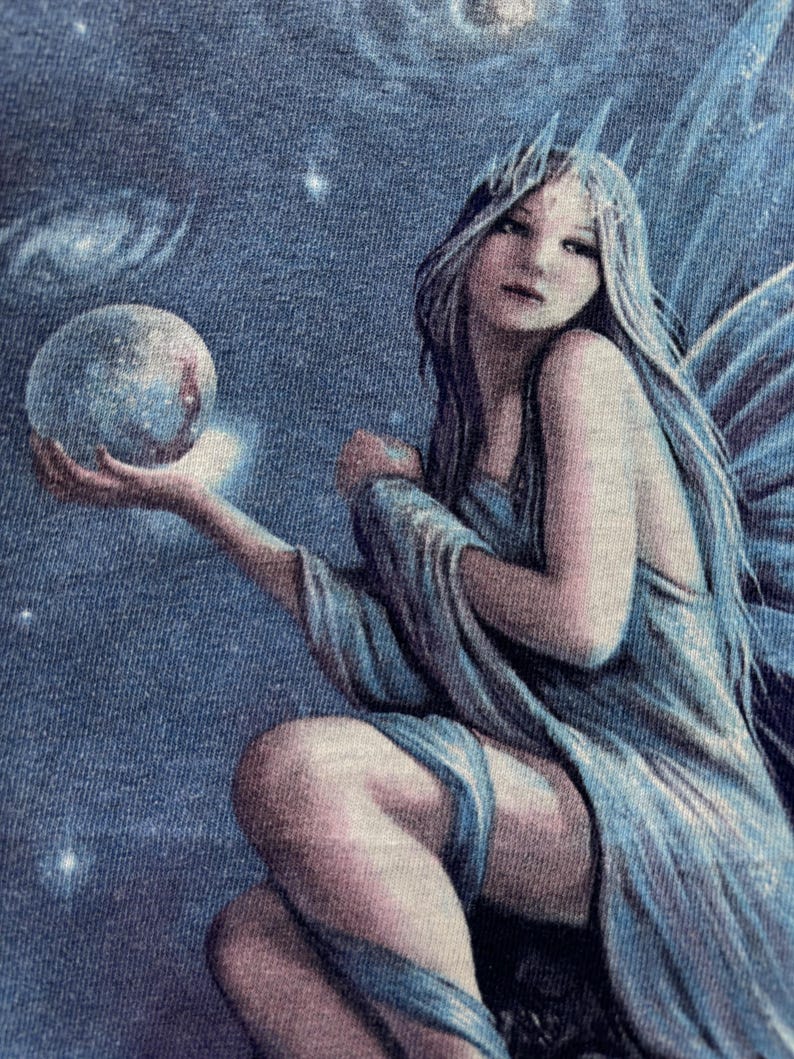 May include: A celestial-themed illustration of a fairy with long, flowing silver hair and blue wings. She is holding a glowing orb, with a starry night sky and galaxies in the background. The fairy is wearing a flowing blue gown.