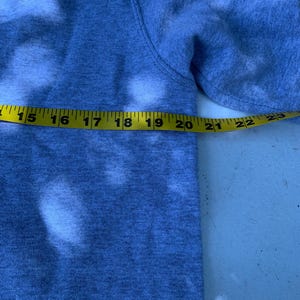 May include: A gray sweatshirt with a yellow measuring tape stretched across the sleeve. The tape measures from 15 to 23 inches. The sweatshirt has white bleached spots.