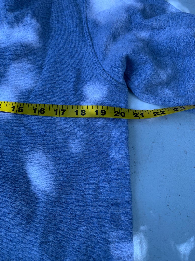 May include: A gray sweatshirt with a yellow measuring tape stretched across the sleeve. The tape measures from 15 to 23 inches. The sweatshirt has white bleached spots.