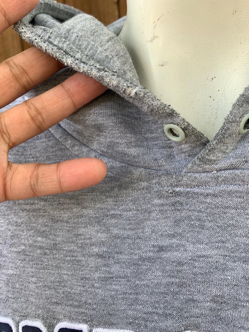 May include: Close-up of a gray hoodie with a drawstring hood. The hood is lined with a lighter gray fabric and has two eyelets. The fabric appears to be a soft, knit material.