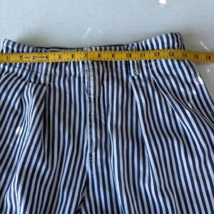 Puede incluir: Primer plano de pantalones a rayas azules y blancas. Una cinta m&eacute;trica amarilla se coloca sobre la parte superior de los pantalones, mostrando una medida de aproximadamente 38 cm. Los pantalones tienen un frente plisado.