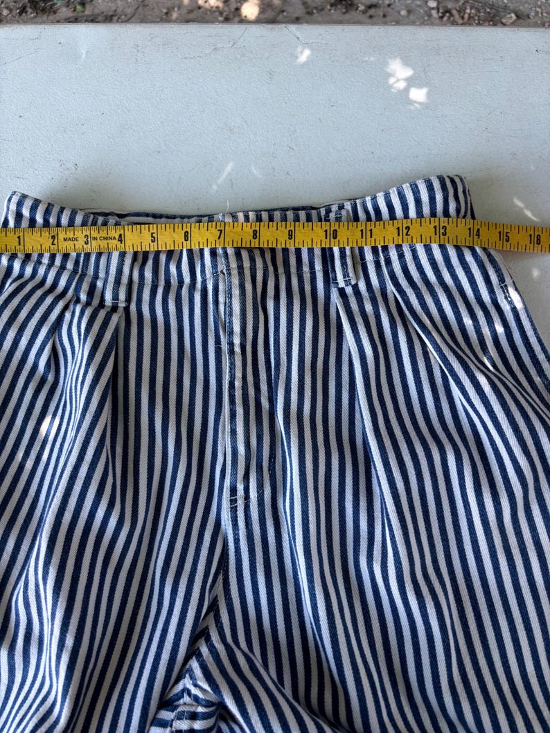 Puede incluir: Primer plano de pantalones a rayas azules y blancas. Una cinta m&eacute;trica amarilla se coloca sobre la parte superior de los pantalones, mostrando una medida de aproximadamente 38 cm. Los pantalones tienen un frente plisado.
