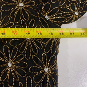 May include: Black sheer fabric with gold and white beading in a floral pattern. The fabric is measured with a tape measure.