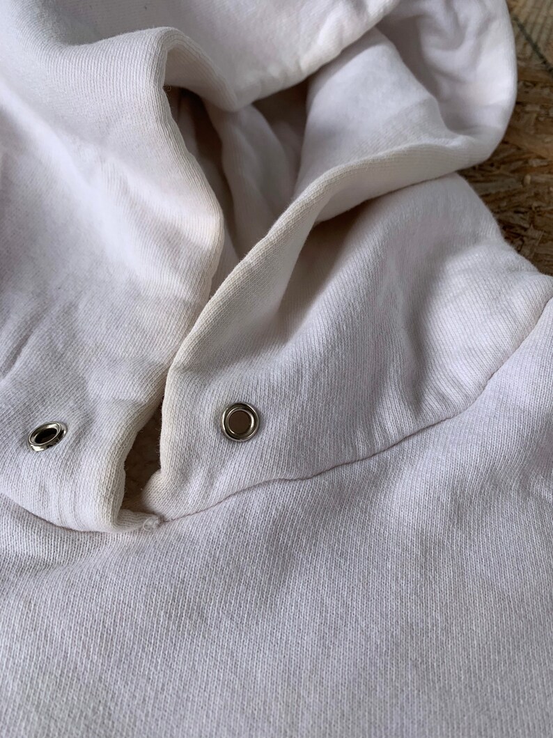 May include: Close-up of a white hooded sweatshirt with two metal eyelets on the hood.