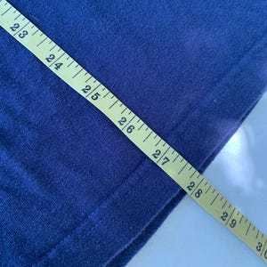 May include: A close-up of a navy blue fabric with a yellow measuring tape. The tape reads 23 to 30 inches.