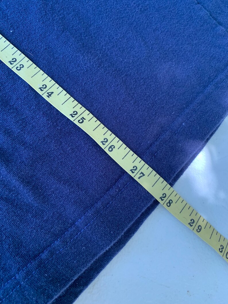 May include: A close-up of a navy blue fabric with a yellow measuring tape. The tape reads 23 to 30 inches.