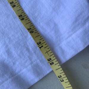 Pu&ograve; includere: Primo piano di un tessuto bianco con un metro a nastro giallo. Il nastro mostra misure da 68,6 cm a 86,4 cm. Il tessuto &egrave; una tela semplice.
