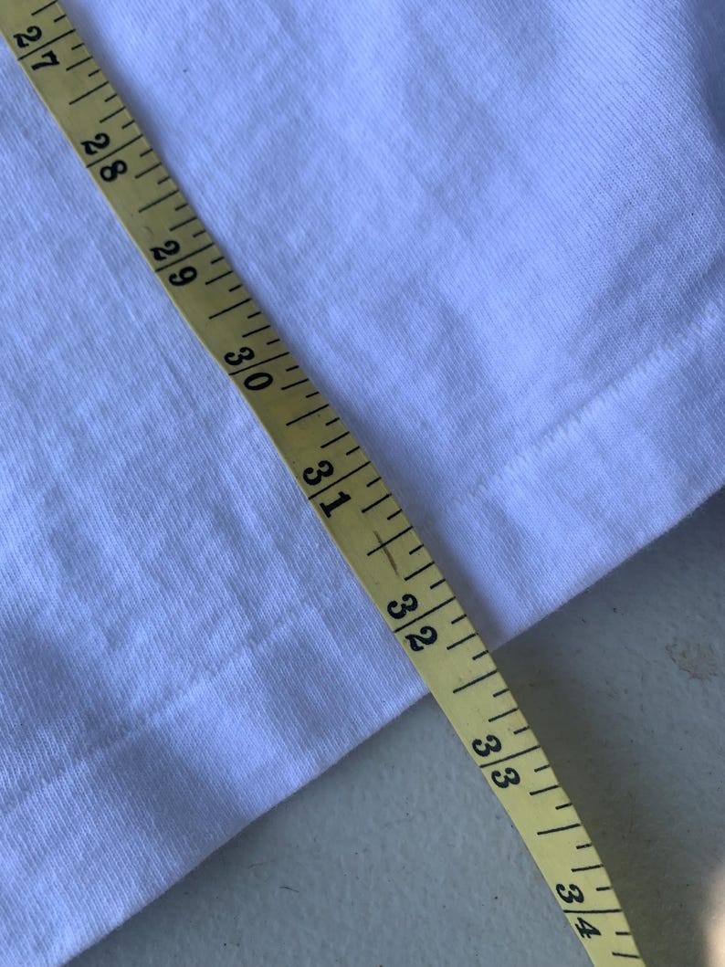 Pu&ograve; includere: Primo piano di un tessuto bianco con un metro a nastro giallo. Il nastro mostra misure da 68,6 cm a 86,4 cm. Il tessuto &egrave; una tela semplice.