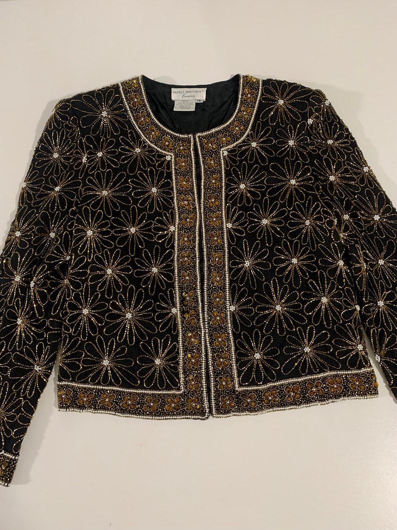 May include: A black beaded jacket with gold and white accents. The jacket features a floral pattern and a front zipper closure.