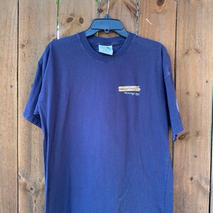 May include: A navy blue t-shirt with a graphic of a wooden sign that reads "Margaritaville Montego Bay".