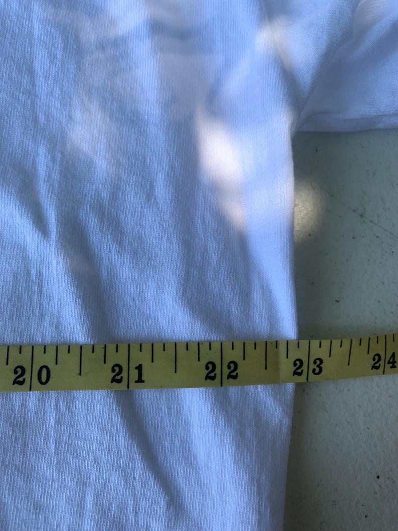 Pu&ograve; includere: Una maglietta bianca con un metro a nastro giallo appoggiato sopra. Il nastro misura da 50,8 cm a 61 cm. Il tessuto ha una trama a coste.