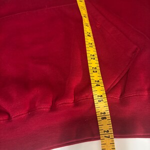 May include: A red hooded sweatshirt with the text "WASHINGTON DC" embroidered in white. A yellow measuring tape is placed over the sweatshirt, showing measurements in inches.