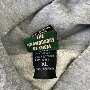 May include: Close-up of a gray hoodie with a tag that reads "THE GRANDDADDY OF THEM." The tag also indicates the hoodie is 80% cotton, 20% polyester, size XL, and made in Vietnam. The hoodie has a drawstring and a light gray color.