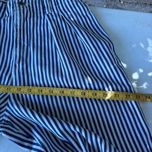 Puede incluir: Pantalones a rayas azules y blancas con cierre de bot&oacute;n. Los pantalones se miden con una cinta m&eacute;trica amarilla, mostrando una longitud de aproximadamente 61 cm.