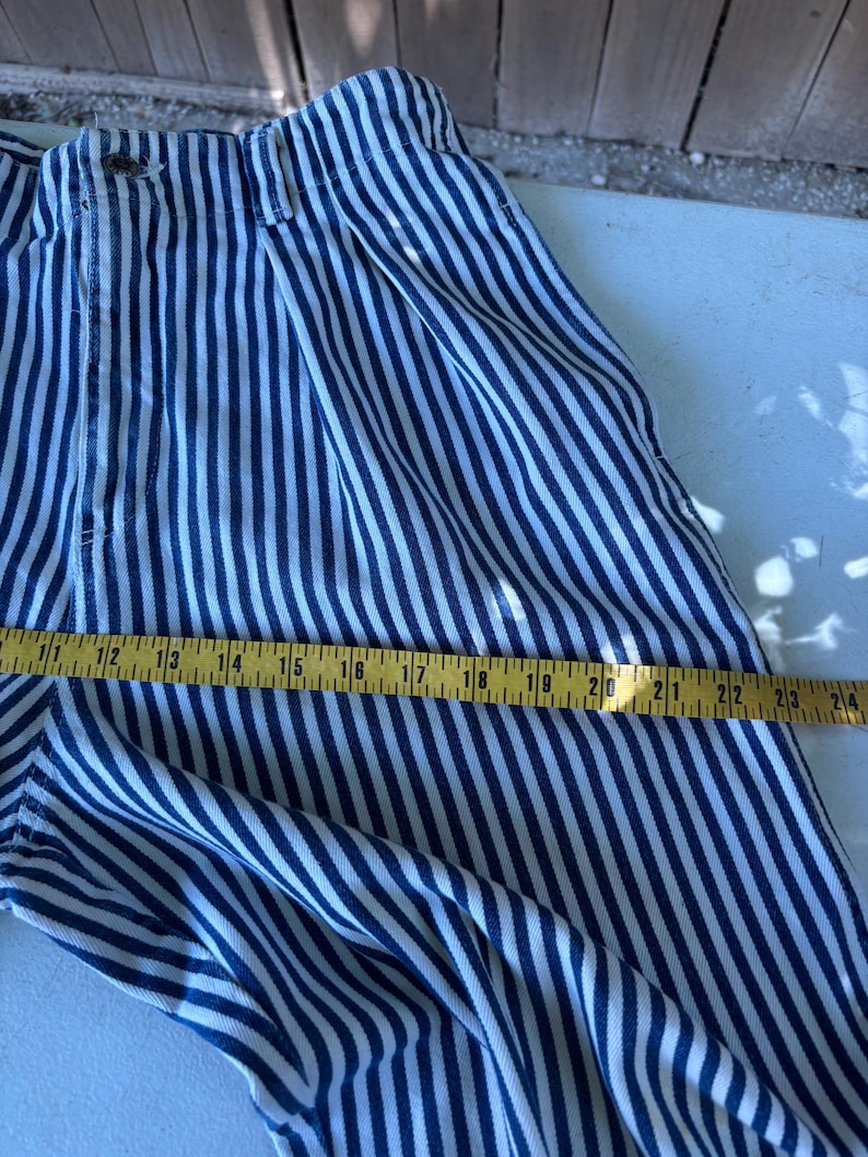 Puede incluir: Pantalones a rayas azules y blancas con cierre de bot&oacute;n. Los pantalones se miden con una cinta m&eacute;trica amarilla, mostrando una longitud de aproximadamente 61 cm.
