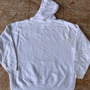 May include: A white hooded sweatshirt with a drawstring hood. The sweatshirt is made of a soft, comfortable fabric and has a relaxed fit.