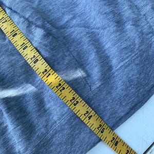 May include: Close-up of a gray fabric with a pocket and a yellow measuring tape. The tape shows measurements from 17 to 28 inches. The fabric appears to be a soft, knit material.