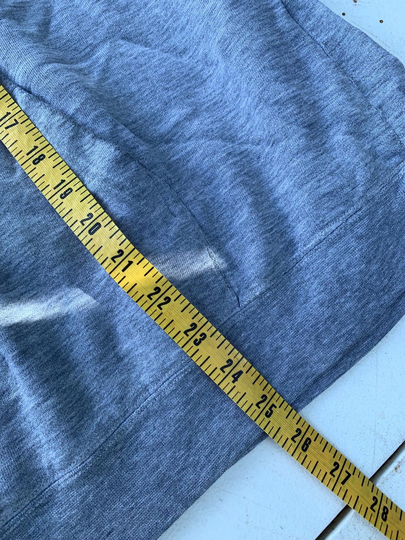 May include: Close-up of a gray fabric with a pocket and a yellow measuring tape. The tape shows measurements from 17 to 28 inches. The fabric appears to be a soft, knit material.