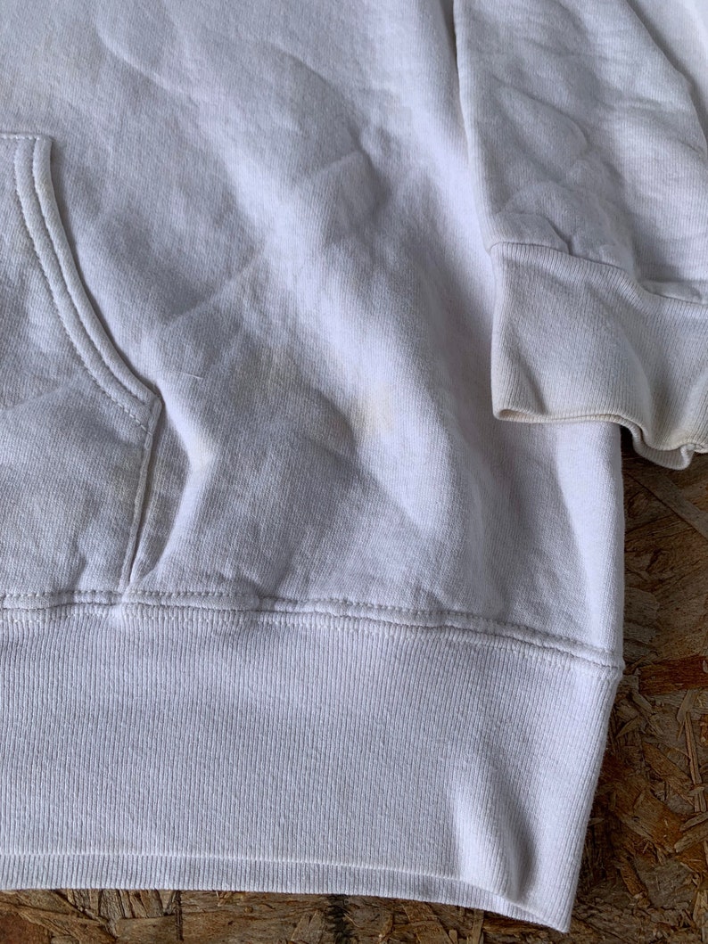 May include: White hooded sweatshirt with a pouch pocket. The sweatshirt has a ribbed hem and cuffs.