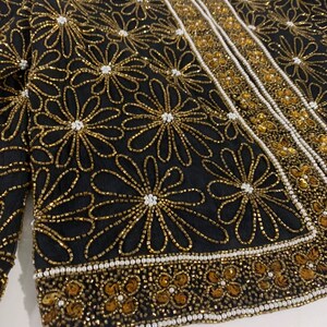 May include: A black beaded jacket with gold and white floral embroidery. The jacket has a beaded trim around the edges.