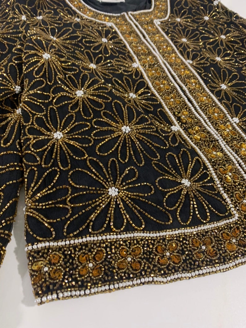 May include: A black beaded jacket with gold and white floral embroidery. The jacket has a beaded trim around the edges.
