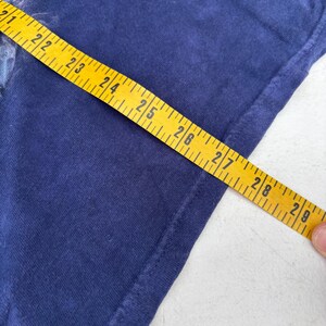 May include: Navy blue t-shirt with a partial graphic and a yellow measuring tape showing 21 to 29 inches. The shirt's fabric is visible, and the tape is held at an angle, indicating a measurement.
