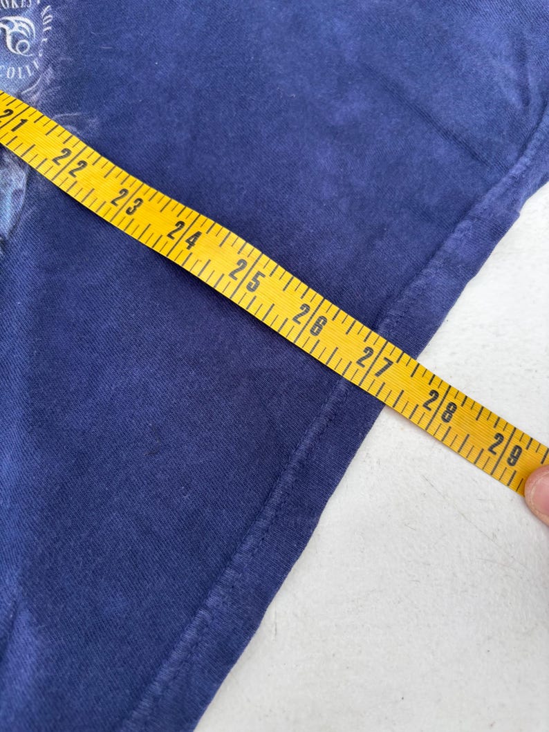 May include: Navy blue t-shirt with a partial graphic and a yellow measuring tape showing 21 to 29 inches. The shirt's fabric is visible, and the tape is held at an angle, indicating a measurement.