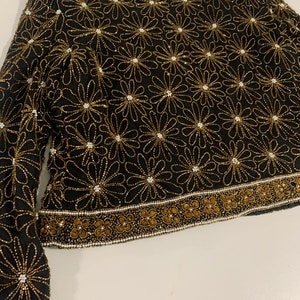 May include: A black beaded top with a floral pattern in gold and white beads. The top has long sleeves and a round neckline.