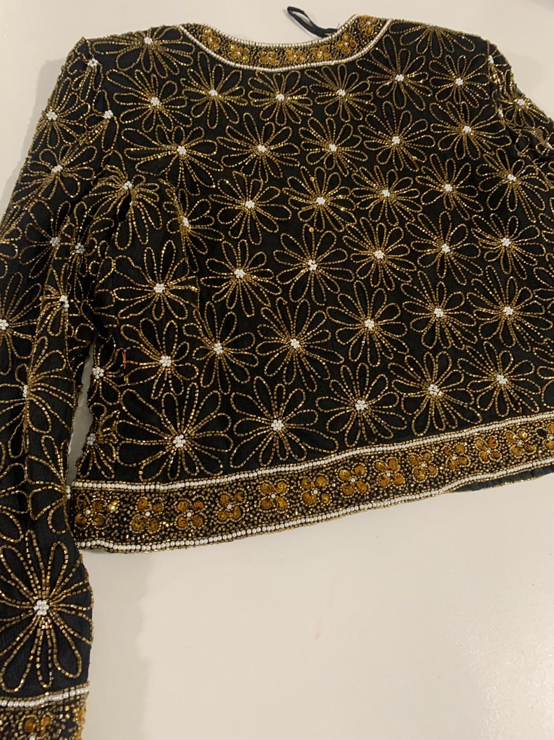 May include: A black beaded top with a floral pattern in gold and white beads. The top has long sleeves and a round neckline.