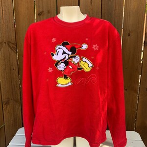 May include: Red long-sleeved fleece sweatshirt with a Mickey Mouse ice skating graphic. Mickey is wearing a Santa hat and is surrounded by snowflakes.