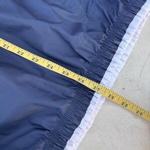 May include: Navy blue garment with a white trim and a yellow measuring tape. The garment has a gathered elastic waist and a small pocket. The measuring tape shows measurements from 21 to 30 inches.