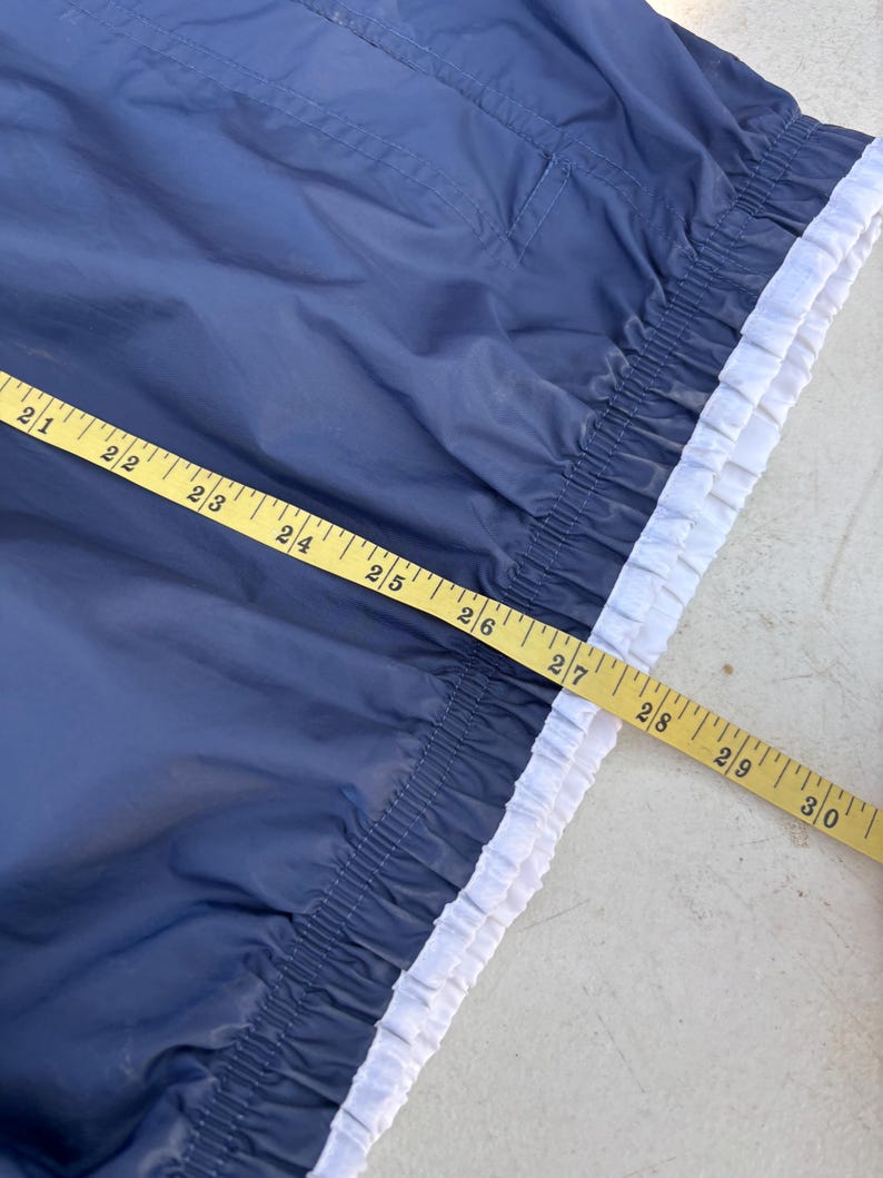 May include: Navy blue garment with a white trim and a yellow measuring tape. The garment has a gathered elastic waist and a small pocket. The measuring tape shows measurements from 21 to 30 inches.